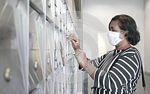 Woman wearing face mask opening metal letter box
