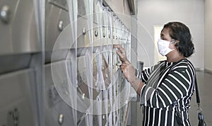 Woman wearing face mask opening metal letter box