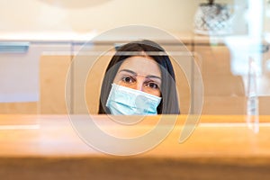 Woman wearing a face mask and sitting behind desk while working at a reception of a spa or health center.