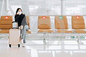 woman wearing face mask sitting on social distancing chair with luggage