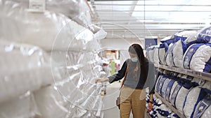 woman wearing face protective mask looking at quality of different mattresses and pillows for bed