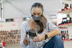 Woman wearing face protective medical mask for protection from virus disease in shoes store during coronavirus pandemia. Woman