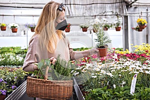 Woman wearing FFP2 face mask and shopping flowers and plants in garden center