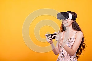 Woman wearing a futuristic looking virtual reality headset goggles in studio over yellow background