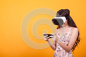 Woman wearing a futuristic looking virtual reality headset goggles in studio over yellow background