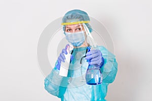 Woman wearing gloves, biohazard protective suit, face shield and mask with hand sanitizer bottle and disinfection gel. corona