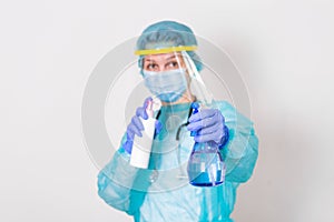 Woman wearing gloves, biohazard protective suit, face shield and mask with hand sanitizer bottle and disinfection gel. corona