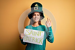 Woman wearing green hat celebrating st patricks day holding banner with saint patrick message doing ok sign with fingers,