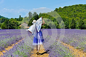 A woman wearing a hat and beautiful lavender dress walking on the path in the lavender fields. Provence, France