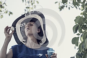 Woman wearing hat blowing bubbles under tree