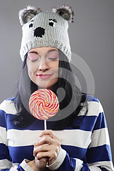 Woman wearing hat looking into the camera and holding a lollipo