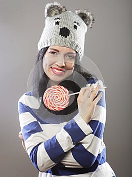 Woman wearing hat looking into the camera and holding a lollipo