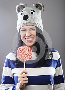 Woman wearing hat looking into the camera and holding a lollipo