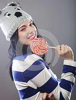 Woman wearing hat looking into the camera and holding a lollipo