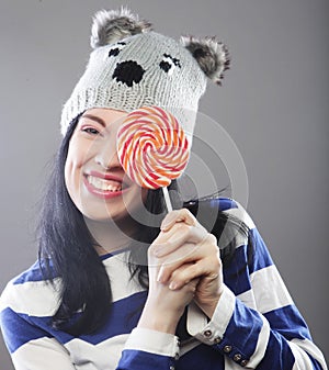 Woman wearing hat looking into the camera and holding a lollipo