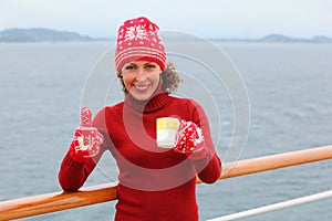 Woman wearing in hat and mittens holds cup of tea