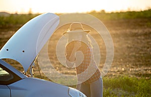 Woman wearing hat stranded in field with broken down car