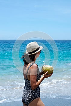 A woman wearing a hat and a swimming suit walking along a beautiful coastline, Bali
