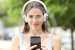 Woman wearing headphones holding phone looking at you