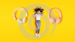 Woman Wearing Headphones Lying Near Huge Earphones Listening Music, Studio