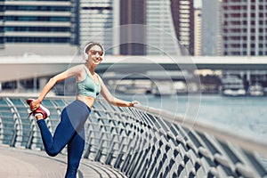 Woman wearing headphones stretches the quadriceps muscles of the thigh and warms up before intense running workout on the