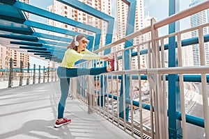 Woman wearing headphones stretches the quadriceps muscles of the thigh and warms up before intense running workout on the