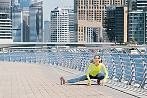 Woman wearing headphones stretches and warms up after an intense running workout on the embankment in Dubai Marina