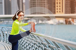 Woman wearing headphones stretches and warms up after an intense running workout on the embankment in Dubai Marina