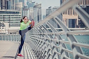 Woman wearing headphones stretches and warms up after an intense running workout on the embankment in Dubai Marina