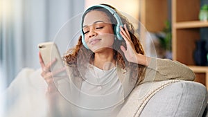 Woman wearing headphones and using a phone to listen to her music while relaxing on a sofa at home. Carefree female