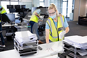 Woman wearing hi vis vest and face mask cleaning the office using disinfectant