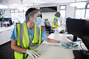 Woman wearing hi vis vest and face mask cleaning the office using disinfectant