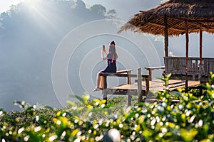 Woman wearing hill tribe dress sitting on the hut in green tea field.