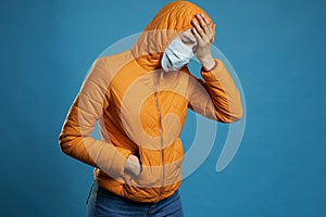 Woman wearing hood in a protective face mask and coat over blue background. Model girl in medical mask and spring outfit