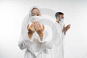 Woman wearing ihram clothes and mask performing al fatihah prayer photo