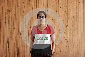 Woman wearing Iraq flag color shirt and standing with two hands in pant pockets on the wooden wall background