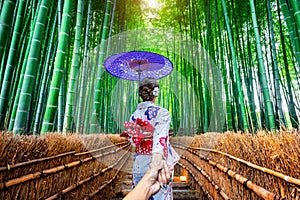 Woman wearing japanese traditional kimono holding man`s hand and leading him to Bamboo Forest in Kyoto, Japan photo