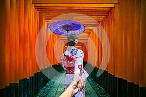 Woman wearing japanese traditional kimono holding man`s hand and leading him to gates walkway at fushimi inari taisha shrine