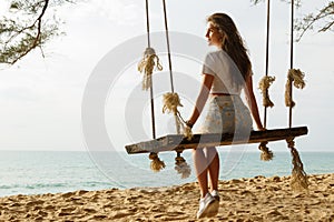 Woman wearing jeans shorts relax on the swing on the beach