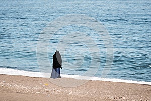 Woman wearing a jilbab watching the sea on the beach on an overcast day
