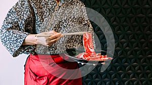 Woman wearing kimono holding rare slice Wagyu A5 beef by chopsticks for boiling in Sukiyaki hot pot photo