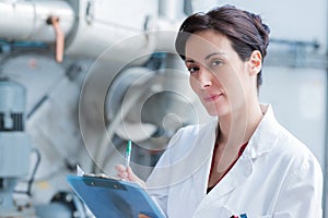 woman wearing labcoat and holding clipboard in industrial setting