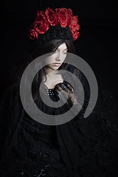 Woman wearing lace dress with a red rose headdress against a black backdrop