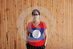 Woman wearing Laos flag color shirt and standing with two hands in pant pockets on the wooden wall background