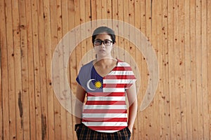 Woman wearing Malaysia flag color shirt and standing with two hands in pant pockets on the wooden wall background