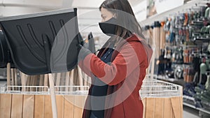 Woman wearing mask and gloves in shop buys a snow shovel