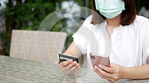 Woman wearing mask making online payment, shopping online, food delivery paying with credit card using smart phone amid