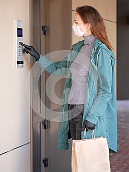 Woman wearing a mask for prevent virus with shopping bags dials the door code