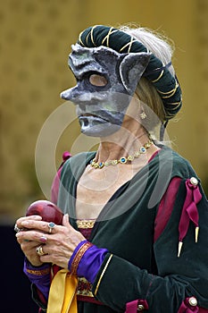 Woman wearing a mediaeval mask while holding a red apple photo