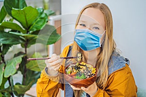 Woman wearing a medical mask during COVID-19 coronavirus eating Raw Organic Poke Bowl with Rice and Veggies close-up on